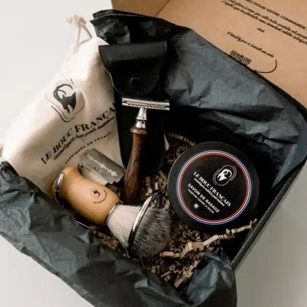 Coffret de rasage traditionnel contenant un rasoir en bois, un blaireau, du savon de rasage Le Bouc Français, et une pochette en tissu, présentés dans une boîte élégante avec des éléments d’emballage naturels.