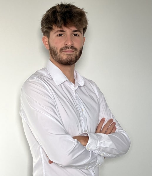 Portrait du créateur de Monsieur à Barbe. Un homme barbu, aux cheveux châtains et chemise blanche, pose de biais avec les bras croisés, regardant l'objectif.